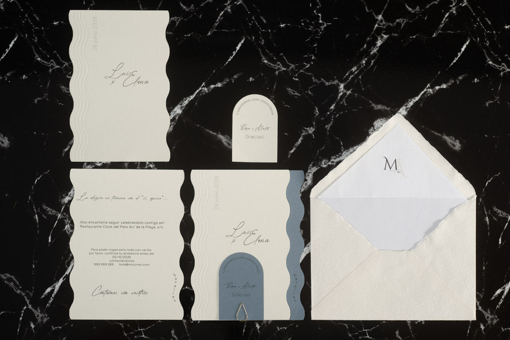 Set completo de la invitación de boda Berilio en color azul: tarjetas onduladas con detalles del evento, tarjeta de agradecimiento y sobre artesanal blanco con forro personalizado.