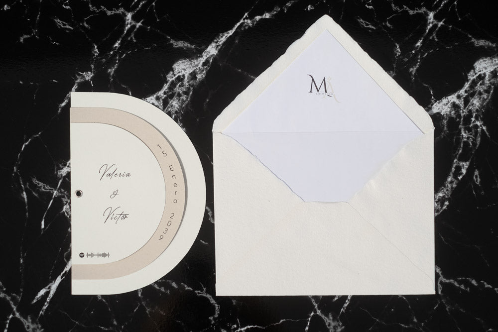 Invitación de boda modelo Cuarzo en color beige, semicircular cerrada, con los nombres de los novios y la fecha del enlace impresa en el borde exterior. Con sobre blanco forrado.