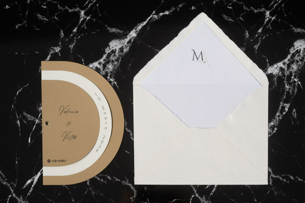 Invitación de boda modelo Cuarzo en color beige, semicircular cerrada, con los nombres de los novios y la fecha del enlace impresa en el borde exterior.
Con sobre blanco con forro.