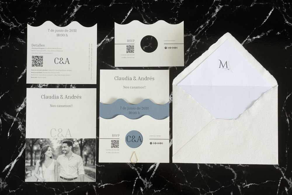 Set completo de la invitación de boda Jade en color azul, con tarjeta principal ondulada, tarjeta de detalles, tarjeta RSVP, tarjeta con fotografía de los novios y sobre artesanal con forro interior blanco.