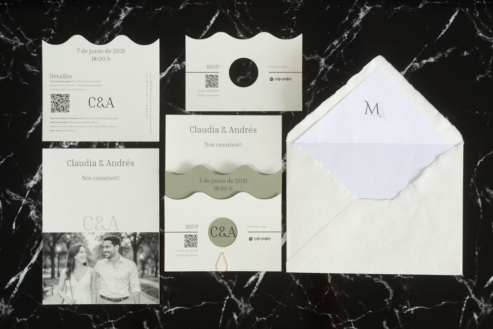 Set completo de la invitación de boda Jade en color verde oliva, compuesto por tarjeta principal con diseño ondulado, tarjeta de detalles, tarjeta RSVP, fotografía de los novios y sobre artesanal con forro interior blanco.