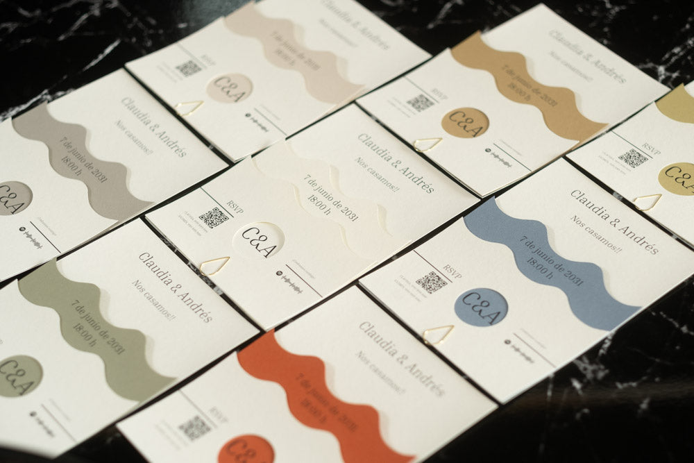 Variedad de invitaciones de boda Jade en diferentes colores: terracota, azul, oliva, arena, marfil, ceniza, miel y beige, todas con diseño ondulado y acabados artesanales.