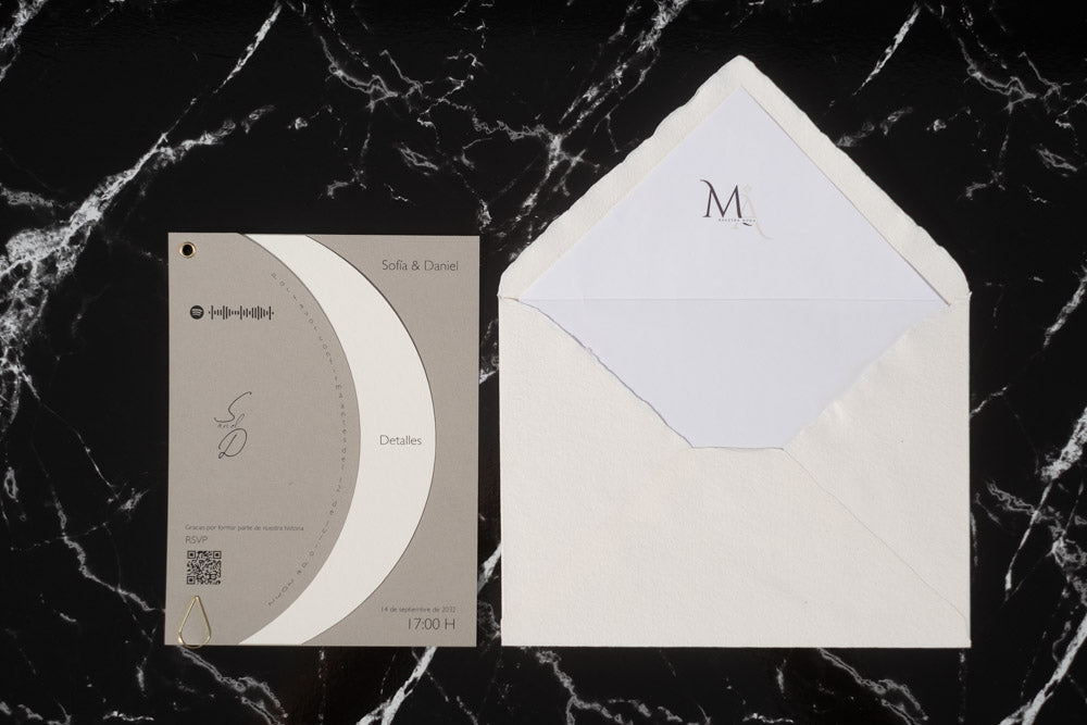 Invitación de boda Larimar color ceniza con tarjeta semicircular giratoria y sobre artesanal con forro interior.