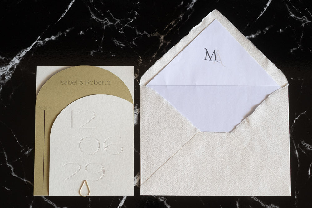 Invitación de boda semicircular en tono miel con textura grabada y tipografía negra, acompañada de sobre artesanal blanco con forro interior personalizado.