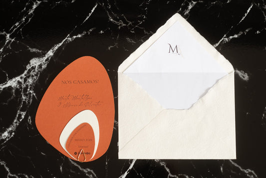 Invitación de boda en formato piedra orgánica color terracota con tarjetas complementarias, junto a sobre artesanal blanco con forro interior.