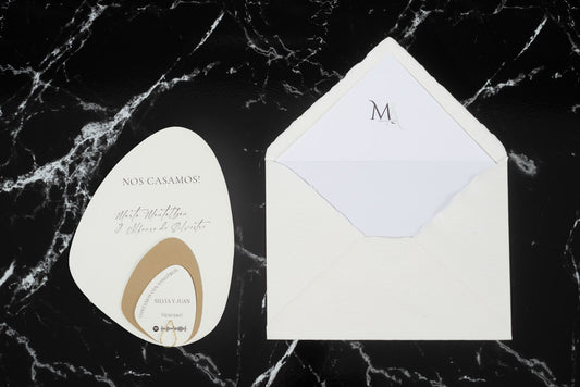 Invitación de boda en formato piedra color blanco roto con tarjetas complementarias, junto a sobre artesanal blanco con forro interior.