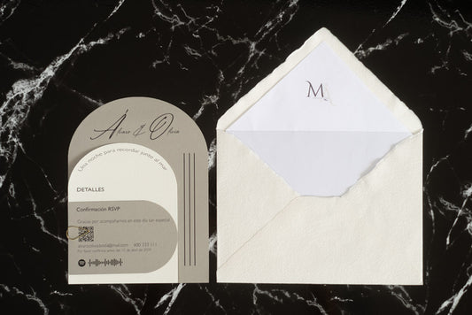 Invitación de boda modelo Aventurina en color ceniza con diseño semicircular moderno, tipografía elegante y detalles en blanco, acompañada de sobre artesanal blanco con forro interior personalizado.
