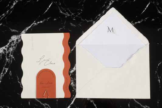 Invitación de boda Berilio en color terracota y blanco con diseño de bordes ondulados, tarjeta adicional con clip dorado y sobre artesanal blanco con forro interior personalizado.