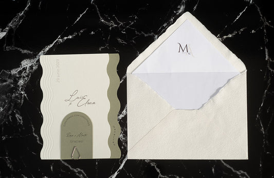Invitación de boda Berilio en tonos verde oliva y blanco con bordes ondulados, tarjeta adicional sujeta con clip dorado y sobre artesanal blanco con forro interior personalizado.