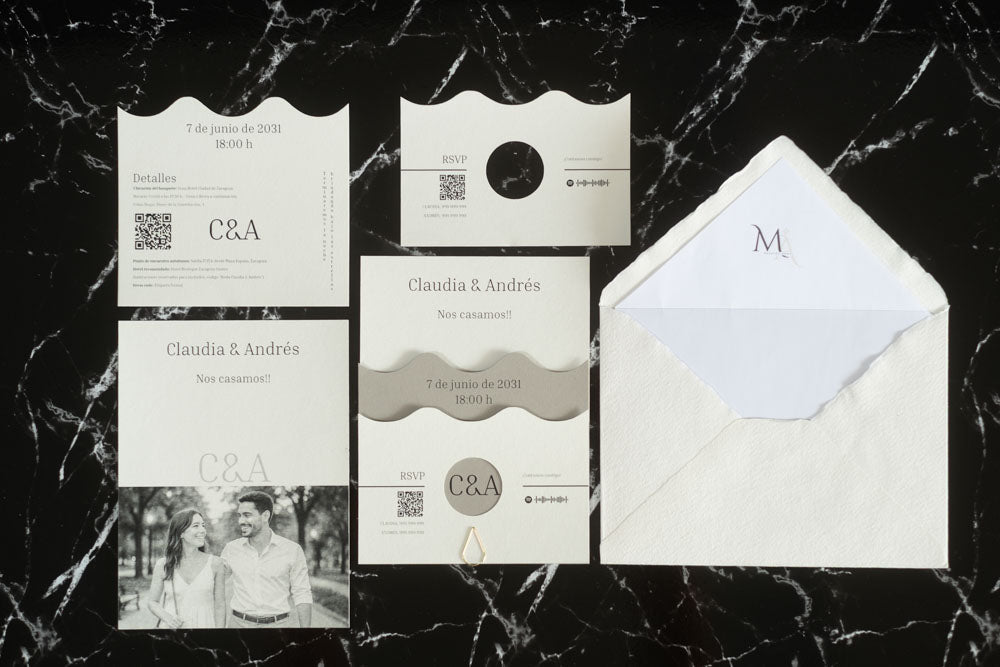 Set completo de la invitación de boda Jade en color gris ceniza, compuesto por tarjeta principal con diseño ondulado, tarjeta de detalles, tarjeta RSVP, tarjeta con fotografía de los novios y sobre artesanal hecho a mano con forro blanco.