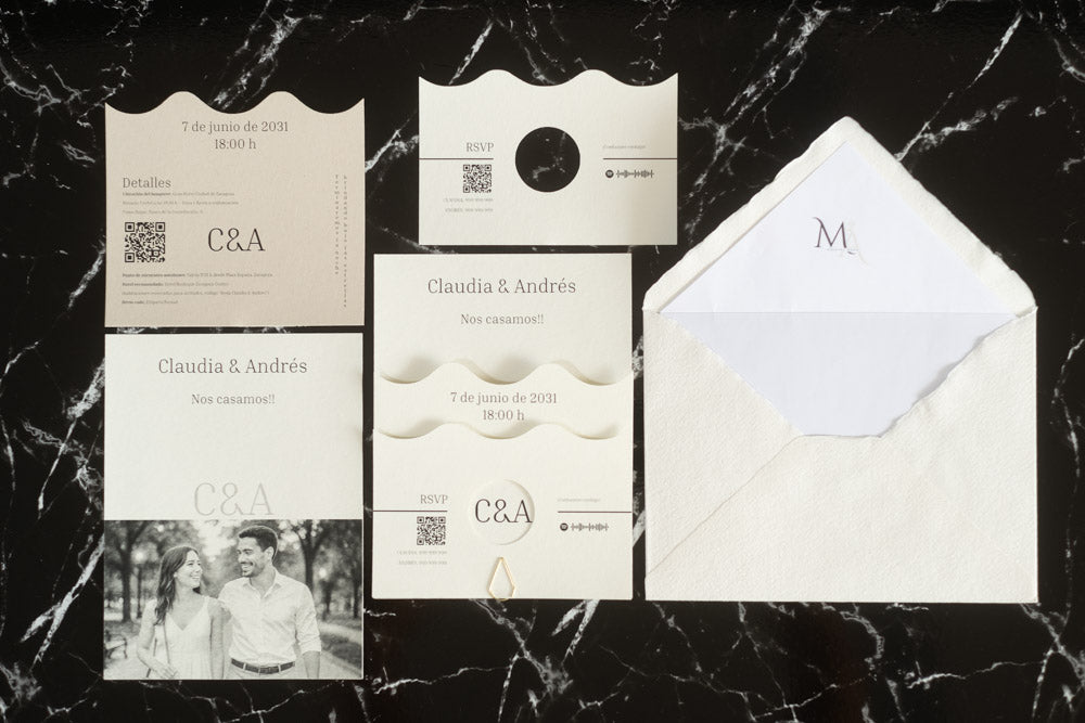 Set completo de la invitación de boda Jade en color marfil, compuesto por tarjeta principal con diseño ondulado, tarjeta de detalles, tarjeta RSVP, tarjeta con fotografía de los novios y sobre artesanal hecho a mano con forro blanco.