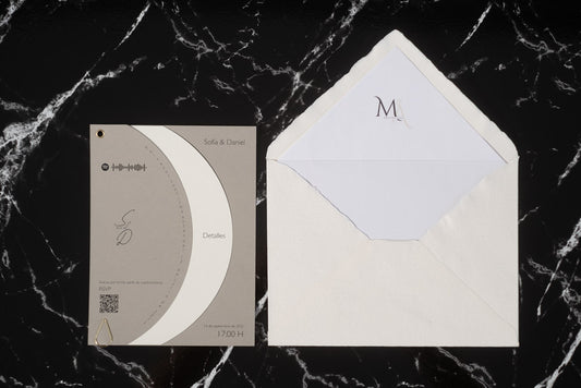 Invitación de boda Larimar color ceniza con tarjeta semicircular giratoria y sobre artesanal con forro interior.