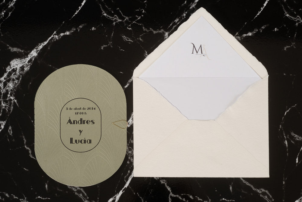Invitación de boda ovalada en tono verde oliva con textura grabada y tipografía negra, acompañada de sobre artesanal blanco con forro interior personalizado.