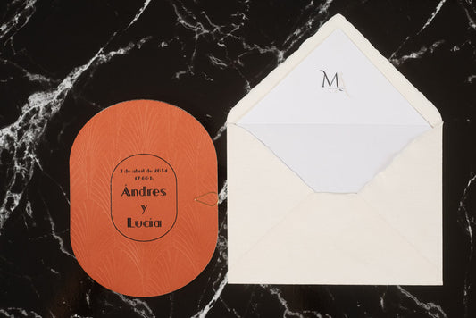 Invitación de boda ovalada en color terracota con detalles grabados y tipografía elegante en negro, junto a sobre artesanal blanco con forro interior personalizado.