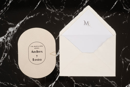 Invitación de boda ovalada en tono marfil con textura grabada y tipografía negra, junto a sobre artesanal blanco con forro interior personalizado.