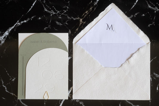 Invitación de boda semicircular en tono verde oliva con textura grabada y tipografía negra, acompañada de sobre artesanal blanco con forro interior personalizado.